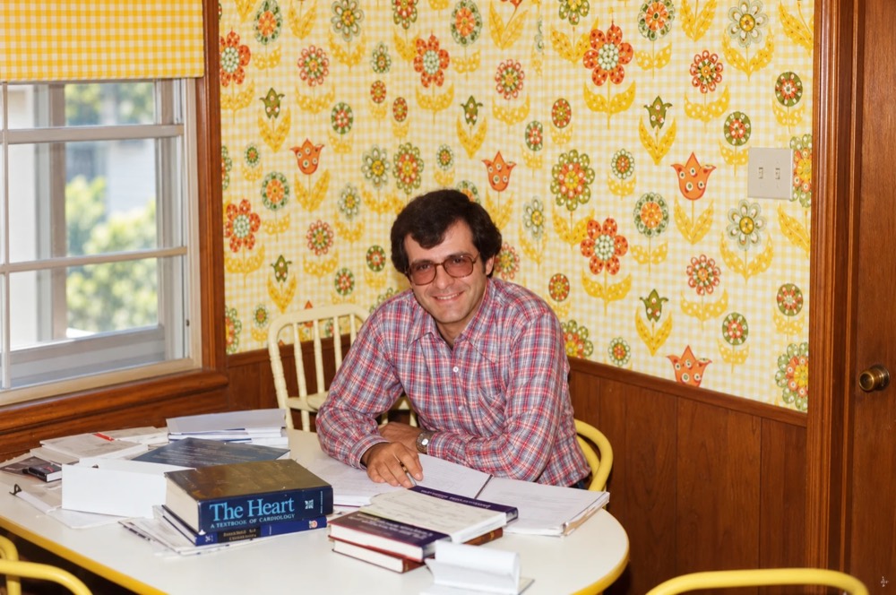 Dr. Antoine Younis, young and smiling, at a table covered with medical books